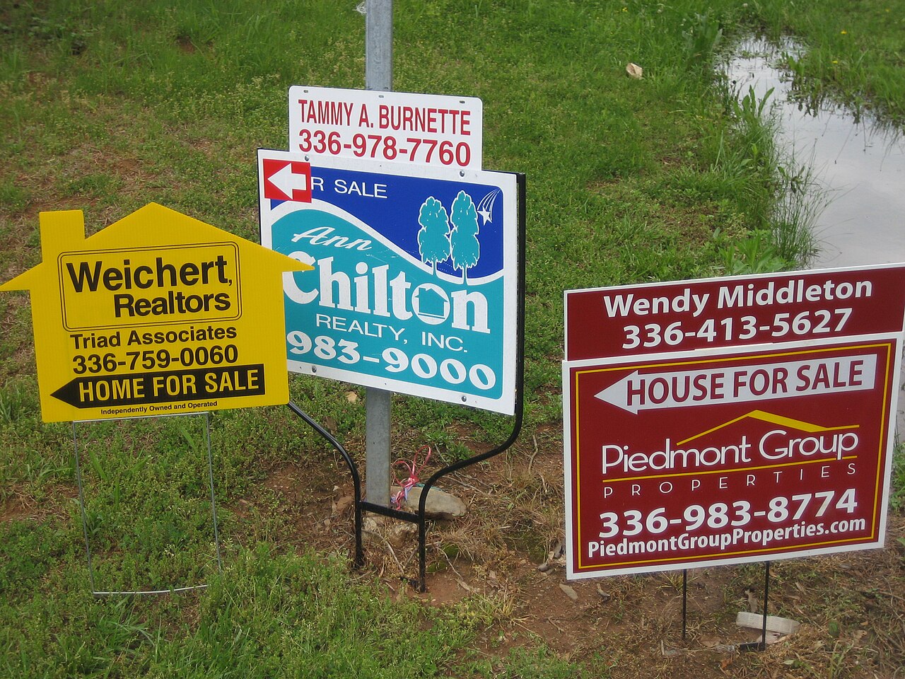 House for sale sign in front of a residential street